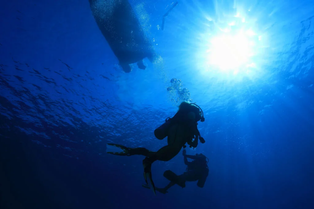 Scuba divers completing a mandatory 15-foot safety stop while holding a surface marker buoy line