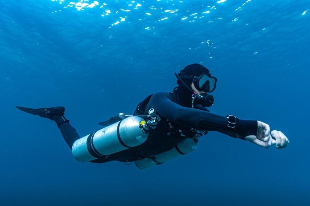 Technical scuba diver swimming in horizontal trim with two side-slung aluminum tanks in a sidemount harness